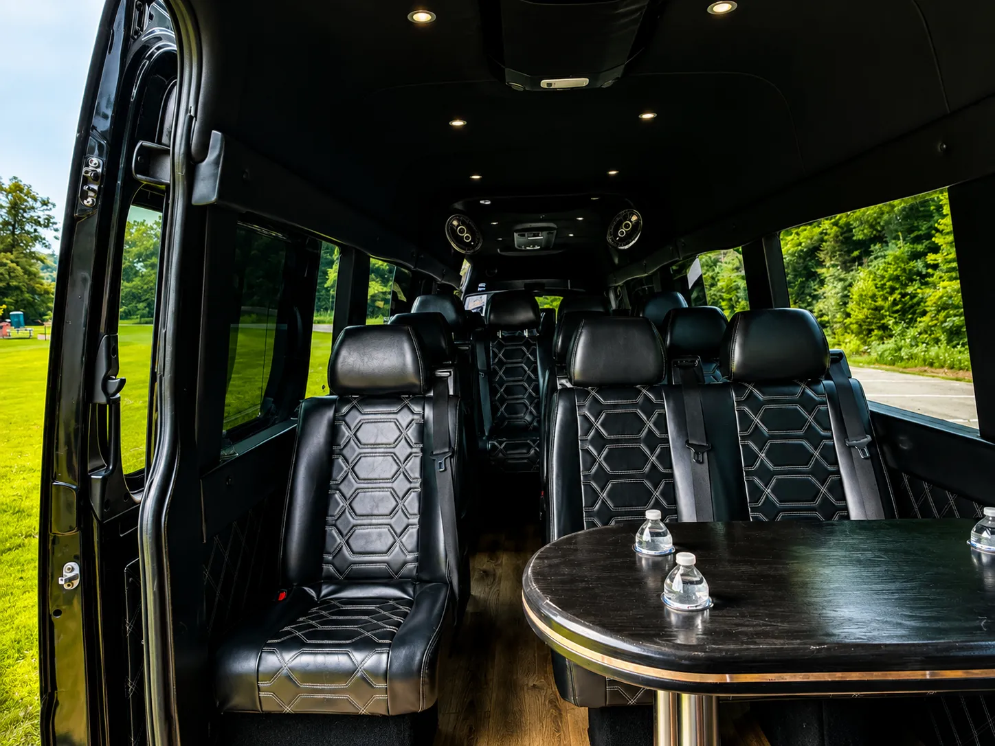 Interior of the Executive Sprinter Van: black leather seats facing a table, the side door open to the kerb