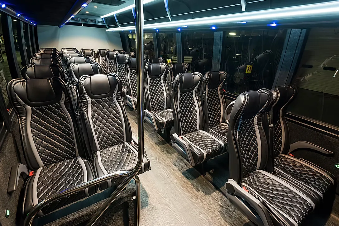 Interior of the Small Coach Bus: quilted black and grey reclining seats along a wood-floored aisle