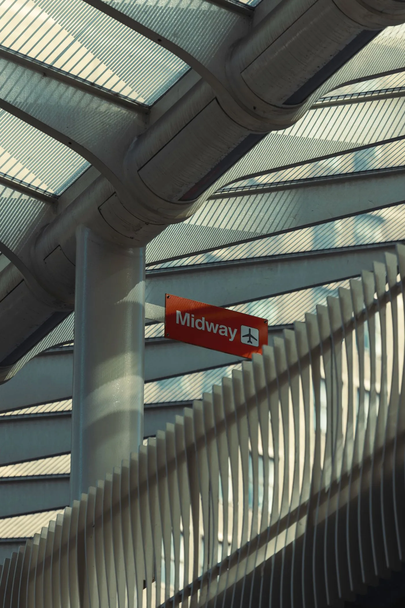 A red Midway airport sign beneath the glass and steel terminal roof